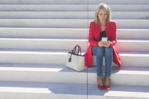 Femme assise sur les escaliers et utilisant un smartphone — Photo de stock