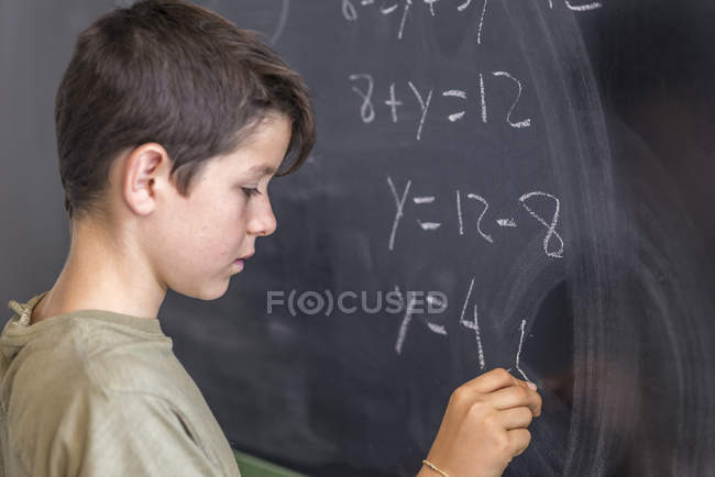 Schoolboy solving a problem on a blackboard. — Stock Photo