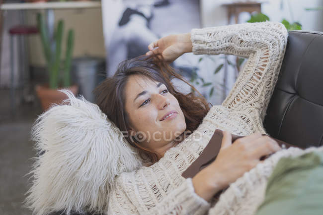 Молода жінка відпочиває на дивані і тримає книгу — стокове фото