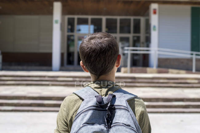 Вид ззаду на шкільного хлопчика, що стоїть і дивиться на будівлю школи — стокове фото