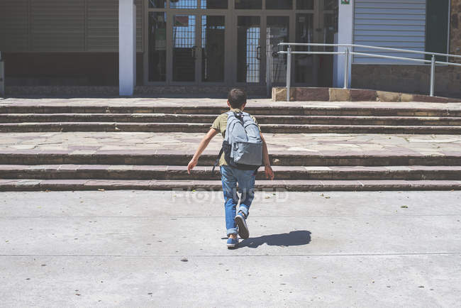 Rear view of schoolboy running at school building — Stock Photo