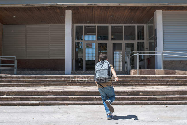 Rear view of schoolboy running at school building — Stock Photo