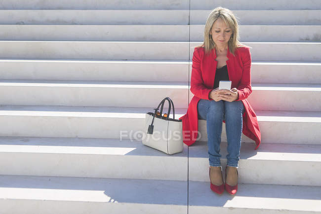 Frau sitzt auf Treppe und nutzt Smartphone — Stockfoto
