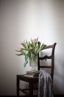 Still life of tulips in vase with pile of books on chair — Stock Photo