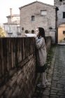 Menina em suéter grande inclinando-se sobre cerca na cidade velha
. — Fotografia de Stock