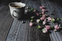 Rose flowers scattered on table with cup of tea — Stock Photo
