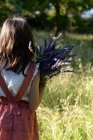 Rear view of girl holding bunch of lavender flowers in countryside garden. — Stock Photo