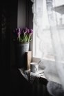 Cubo de tulipanes recién cortados en alféizar de ventana con libro vintage y taza de esmalte - foto de stock