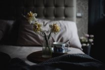 Квіти нарцисів у скляній вазі на дерев'яному підносі з старовинною чашкою у спальні — стокове фото
