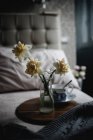 Narzissenblüten in Glasvase auf Holztablett mit Vintage-Tasse im Schlafzimmer — Stockfoto
