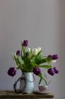 Фіолетові та білі тюльпани в глечику на столі з чашкою кави — стокове фото
