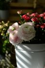 Крупный план розовых лютиков в ведре с цветами роз — стоковое фото