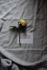 Yellow rose with card on gray linen tablecloth — Stock Photo