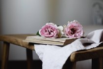 Pink rose flowers on open book on vintage stool, close-up — Stock Photo