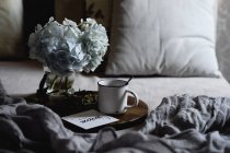 Enamel mug with coffee, white hydrangea flowers on wooden tray in bedroom — Stock Photo