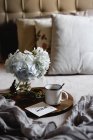 Enamel mug with coffee, white hydrangea flowers on wooden tray in bedroom — Stock Photo