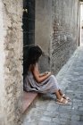 Menina em vestido cinza sentado no alpendre da porta na cidade velha . — Fotografia de Stock