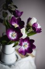 Крупним планом квітуча купа фіолетових тюльпанів в глечику на столі — стокове фото
