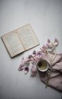 Enamel mug of green tea with tulip petals and open book — Stock Photo