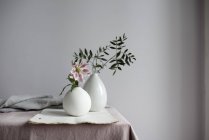 Fleur de lis rose et branches de plantes de feuillage dans des vases sur la table — Photo de stock