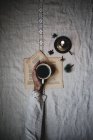 Weiblicher Arm hält Tasse schwarzen Tee auf Tisch mit Buchblättern und Kerze — Stockfoto