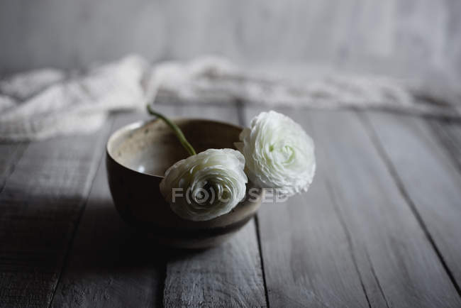 Белые лютики в керамической миске на деревенском полу — стоковое фото