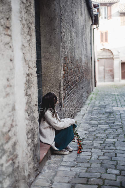 Menina em suéter de tamanho grande sentado no alpendre da porta na cidade velha . — Fotografia de Stock