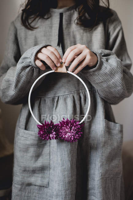 Vista recortada de la chica adolescente sosteniendo anillo de metal con flores de crisantemo - foto de stock