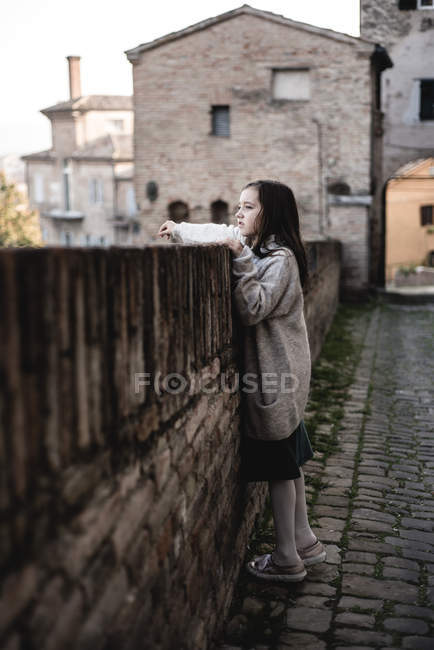 Chica en suéter de gran tamaño apoyado en la cerca en el casco antiguo . - foto de stock