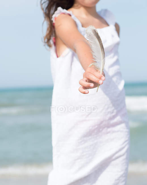 Vista ritagliata della donna che tiene in mano la piuma sulla spiaggia — Foto stock