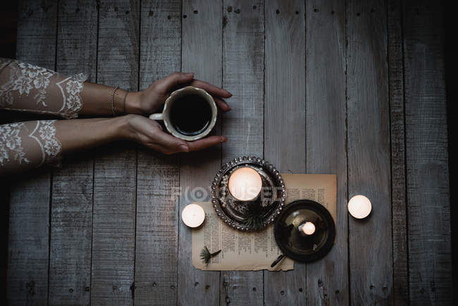 Mãos femininas segurando xícara de café na mesa com velas — Fotografia de Stock