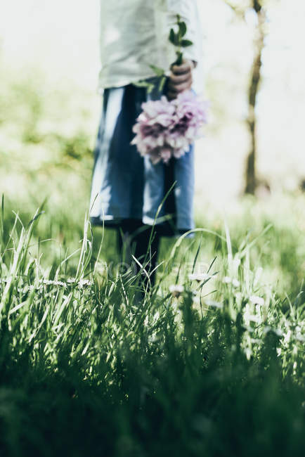 Cropped view of girl holding bunch of flowers in garden — Stock Photo