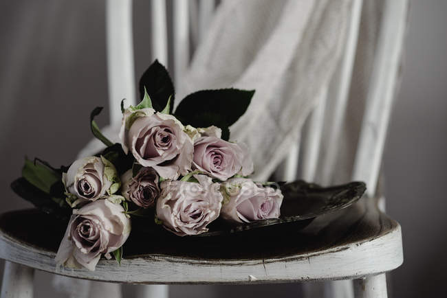 Букет з рожевих троянд у скляній тарілці на дерев'яному стільці — стокове фото