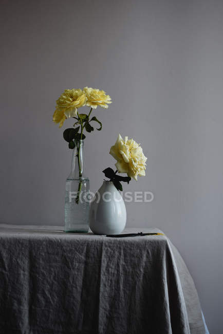 Fleurs roses jaunes dans des vases sur le coin de la table — Photo de stock