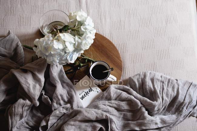 Enamel mug with coffee, white hydrangea flowers on wooden tray on bed — Stock Photo