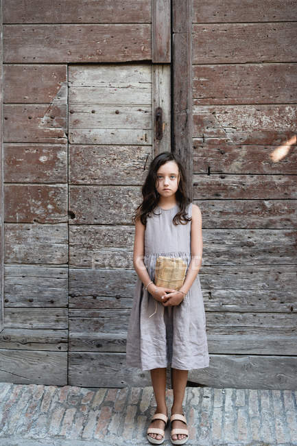 Girl holding bunch of vintage book sheets in front of shabby wooden gate. — Stock Photo