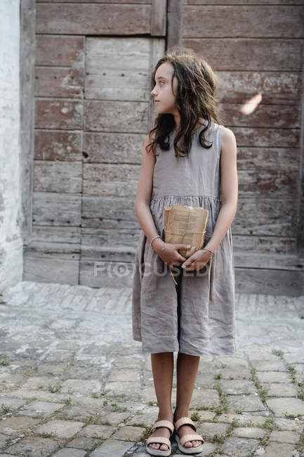 Chica sosteniendo montón de hojas de libro vintage en frente de la puerta de madera de mala calidad . - foto de stock