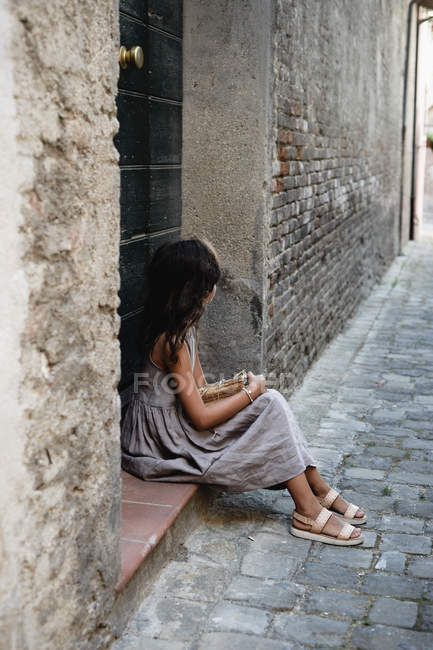 Chica en vestido gris sentado en el porche de la puerta en el casco antiguo . - foto de stock