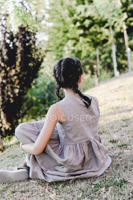 Mädchen in grauem Kleid hockt im sonnigen Garten. — Stockfoto