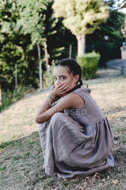 Girl in grey dress crouching in sunny garden. — Stock Photo