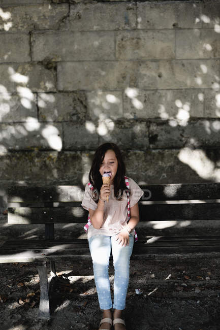 Girl eating ice cream cone on bench in town. — Stock Photo