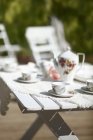 Garden table served with teapot and cups in bright sunlight — Stock Photo