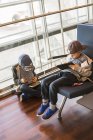 Два мальчика сидят и играют с цифровыми планшетами в зале ожидания — стоковое фото