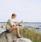 Жінка використовує цифровий планшет на пляжі, фокус на передньому плані — стокове фото
