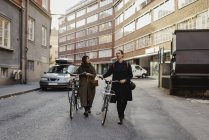 Two people walking with bicycles through street — Stock Photo