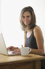 Молода жінка використовує ноутбук і посміхається — стокове фото