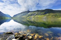 Verdes colinas y cielo nublado reflejándose en el agua del lago - foto de stock