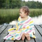 Retrato de menina envolto em toalha sentado no molhe, foco diferencial — Fotografia de Stock