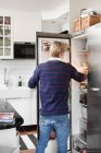 Мальчик-подросток открывает холодильник на кухне — стоковое фото
