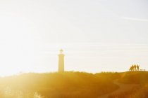 Silhouetted group of people and lighthouse in sunset light — Stock Photo